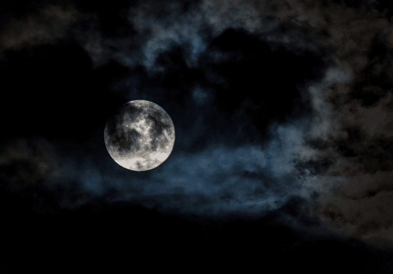 Full moon partially obscured by dark clouds in a night sky.