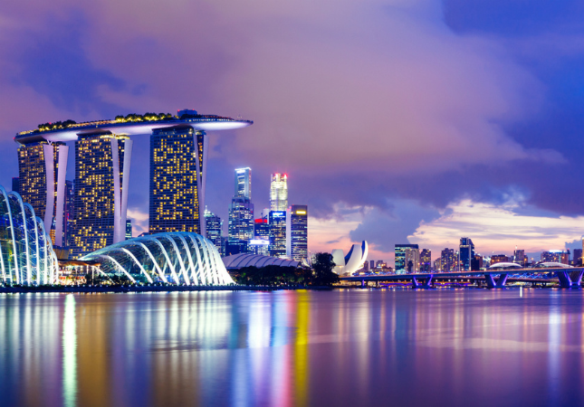 Night view of Marina Bay Sands and surrounding skyline in Singapore, with illuminated buildings reflected in the calm bay water under a twilight sky.