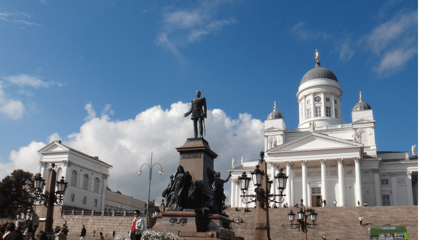 Statue of Alexander II in Senate Square with Helsinki Cathedral and surrounding buildings in the background under a partly cloudy sky.