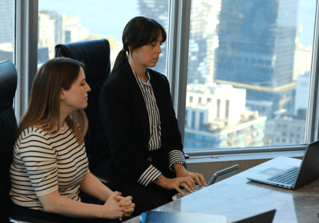 Stenographic court reporter typing on steno machine at conference table with legal professional next to her.