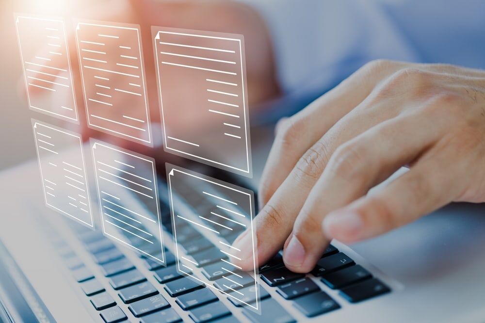Hands typing on a laptop keyboard with digital document icons overlaid, representing working with electronic files or data management.