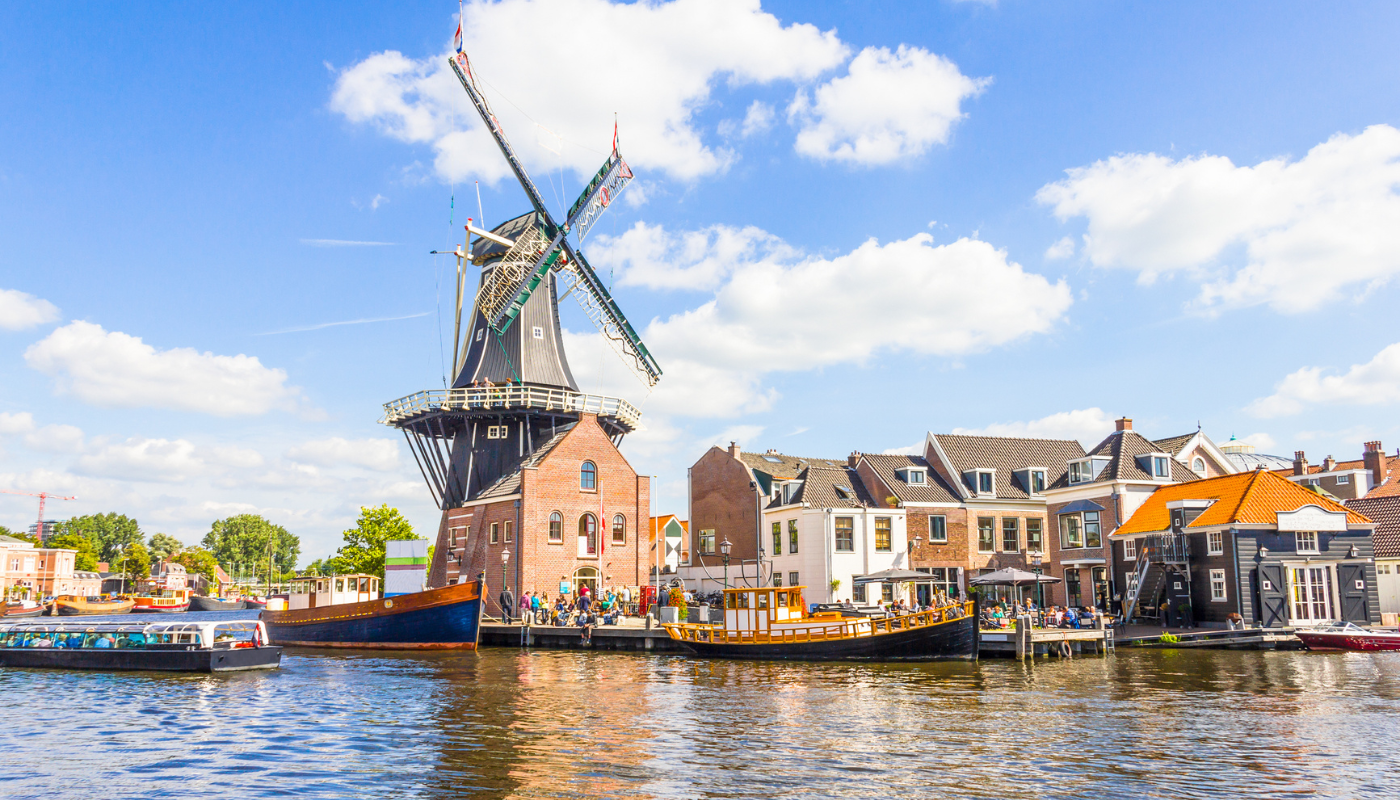 Traditional windmill and surrounding houses along a canal under a blue sky with scattered clouds in the Netherlands.
